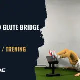 Mężczyzna wykonuje glute bridge z obciążeniem, opierając stopy na ławce. Ćwiczenie na pośladki.