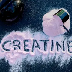 Różowy proszek kreatynowy rozsypany na ciemnym tle, tworzący napis "CREATINE". Obok czajnik i miarka z suplementem. Idealny dla każdego, kto chce poczuć się jak animal.