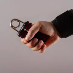 Dłoń z opaską na nadgarstku ściska przyrząd do ćwiczeń na przedramię.
