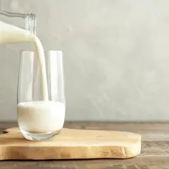 Białe mleko, bogate w białko, leje się z butelki do szklanki. Idealne na zdrowy początek dnia.