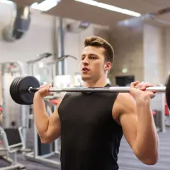 Młody mężczyzna ćwiczy wyciskanie żołnierskie. Ciężar na sztandze wygląda na spory, zastanawiamy się, wyciskanie żołnierskie ile kg?