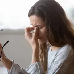 Kobieta z bólem głowy, zastanawia się nad wpływem kreatyny a nadciśnienia. Trzyma okulary.