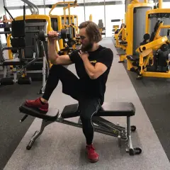 Mężczyzna ćwiczy biceps z hantlem, siedząc na ławce. Dba o balans strukturalny, angażując całe ciało.