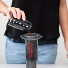 Osoba wsypuje zmieloną kawę do AeroPressu. Dokładne kava kava dawkowanie jest kluczowe dla smaku.