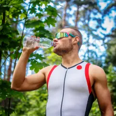 Mężczyzna w sportowym stroju pije wodę z butelki. To najlepsze, co można pić na siłowni, by nawodnić organizm.