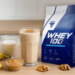 Bananowy koktajl z białkiem z wodą czy mlekiem? Obok opakowanie WHEY 100, masło orzechowe i orzechy.