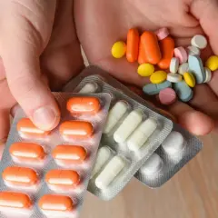 Dłonie trzymają opakowania z lekami i garść tabletek. Niektóre suplementy po terminie przydatności mogą być niebezpieczne.
