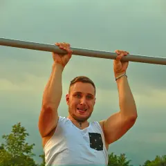 Mężczyzna z uśmiechem wykonuje podciąganie na drążku. To jego plan na dziś, by wzmocnić mięśnie.