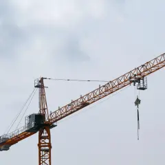 Pomarańczowy żuraw budowlany, jakby w ćwiczeniu, rozpościera swoje ramię na tle pochmurnego nieba.