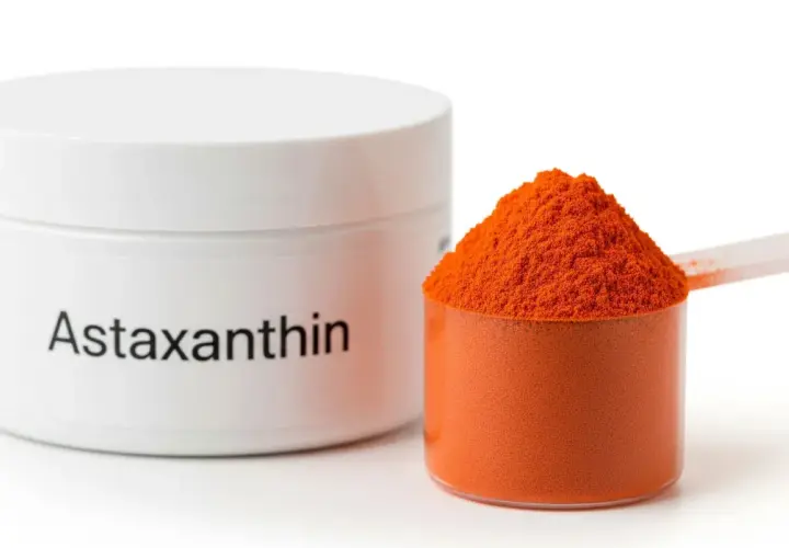 Sypka astaksantyna w pomarańczowym kolorze, obok białego pojemnika z napisem "Astaxanthin". Informacje o potencjalnych astaksantyna skutki uboczne mogą być na etykiecie.