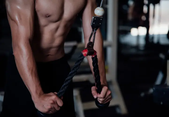 Mężczyzna wykonuje wyciskanie na triceps na siłowni, skupiając się na budowaniu masy mięśniowej ramion.