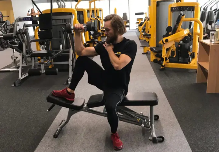 Mężczyzna ćwiczy biceps z hantlem, siedząc na ławce. Dba o balans strukturalny, angażując całe ciało.