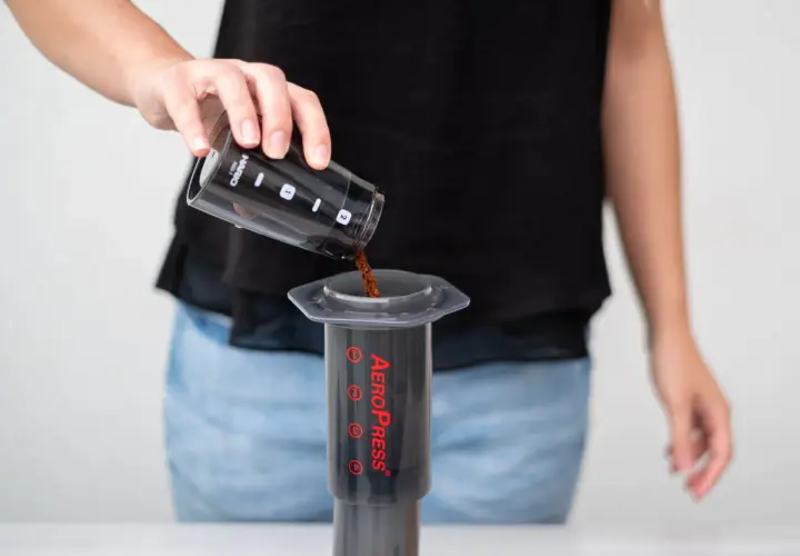 Osoba wsypuje zmieloną kawę do AeroPressu. Dokładne kava kava dawkowanie jest kluczowe dla smaku.