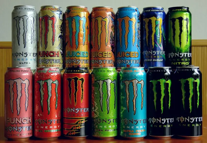 Rząd puszek napojów energetycznych Monster Energy. Różne smaki i warianty, w tym Ultra, Pipeline Punch, Zero Sugar, Lewis Hamilton, Nitro. Skład Monster Energy jest zróżnicowany.