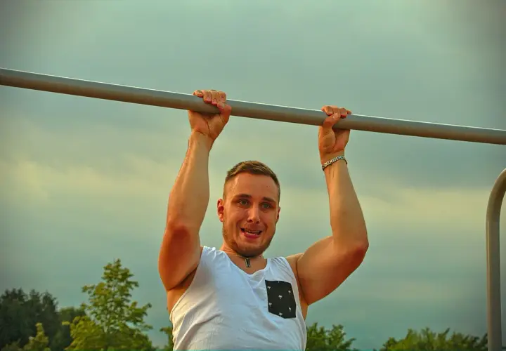Mężczyzna z uśmiechem wykonuje podciąganie na drążku. To jego plan na dziś, by wzmocnić mięśnie.
