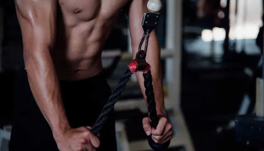 Mężczyzna wykonuje wyciskanie na triceps na siłowni, skupiając się na budowaniu masy mięśniowej ramion.
