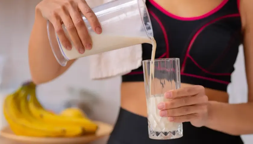 Kobieta w sportowym topie nalewa odżywkę bananową do szklanki. Różne rodzaje odżywek to klucz do regeneracji po treningu.