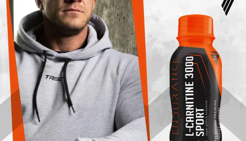 Mężczyzna w szarej bluzie z kapturem obok butelki L-Carnitine 3000 Extreme Shot o smaku gruszka-jabłko.