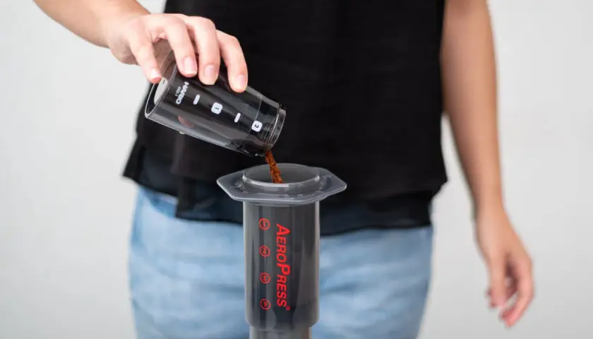 Osoba wsypuje zmieloną kawę do AeroPressu. Dokładne kava kava dawkowanie jest kluczowe dla smaku.