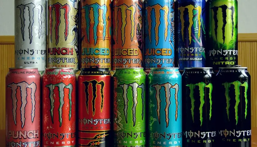 Rząd puszek napojów energetycznych Monster Energy. Różne smaki i warianty, w tym Ultra, Pipeline Punch, Zero Sugar, Lewis Hamilton, Nitro. Skład Monster Energy jest zróżnicowany.