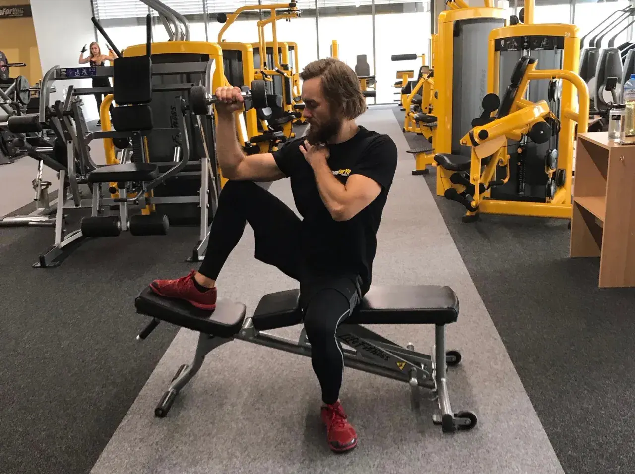 Mężczyzna ćwiczy biceps z hantlem, siedząc na ławce. Dba o balans strukturalny, angażując całe ciało.