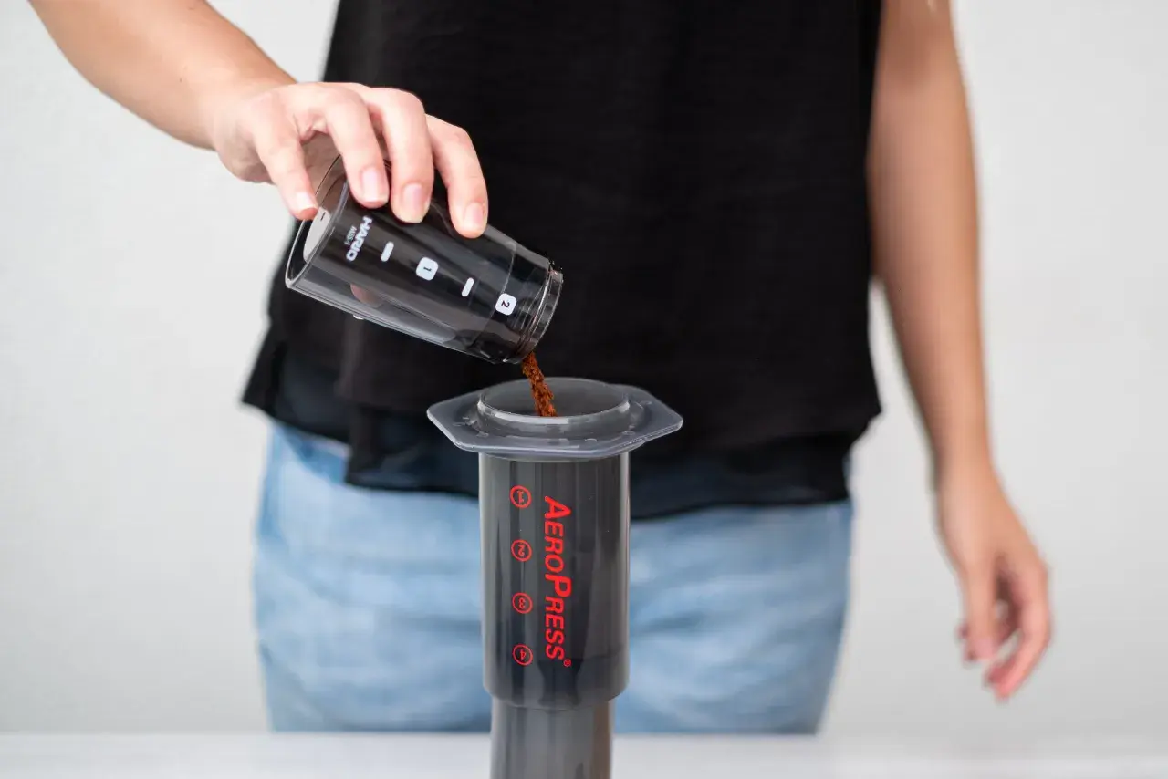 Osoba wsypuje zmieloną kawę do AeroPressu. Dokładne kava kava dawkowanie jest kluczowe dla smaku.