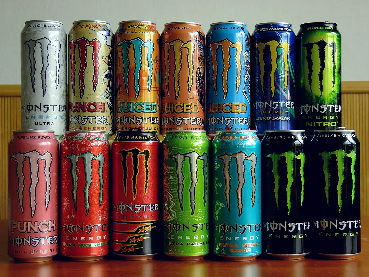 Rząd puszek napojów energetycznych Monster Energy. Różne smaki i warianty, w tym Ultra, Pipeline Punch, Zero Sugar, Lewis Hamilton, Nitro. Skład Monster Energy jest zróżnicowany.