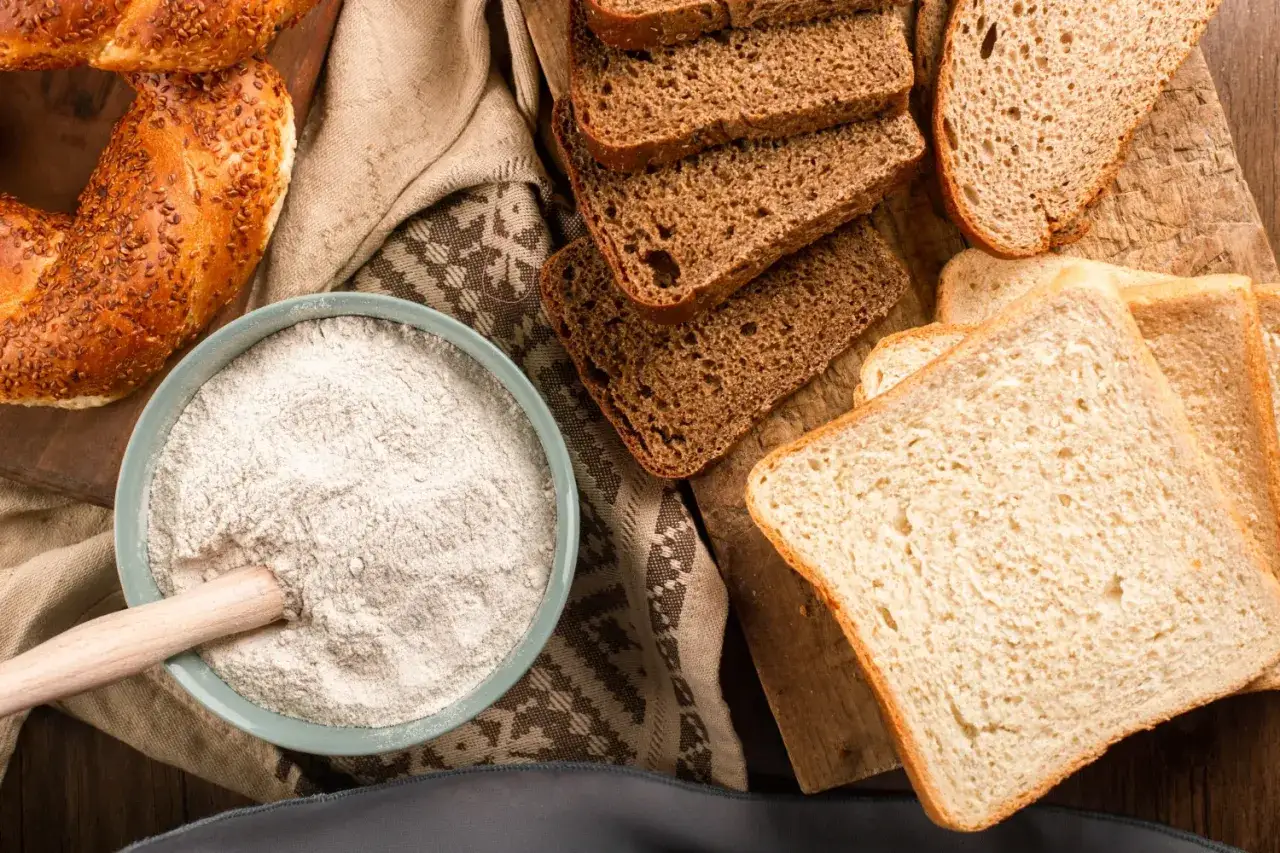 Mąka w misce, kromki chleba i bajgiel. Wszędzie tam, gdzie jest mąka pszenna, jest też gluten.
